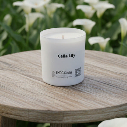 white candle jar on a small wooden table in a field of Calla Lily