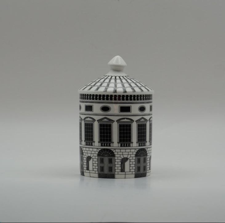 A small cylindrical lidded box or container with a detailed architectural building design in black and white, set against a plain gray studio background.