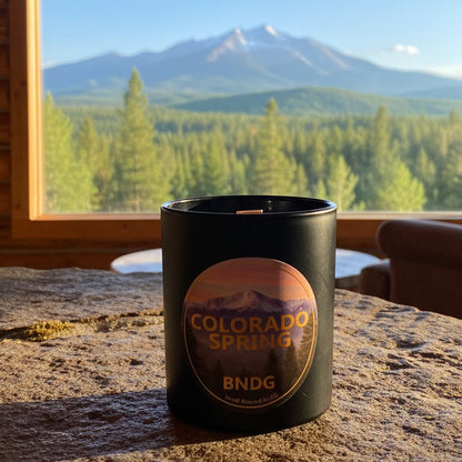 Candle jar with "Colorado Spring"-scent on a stone table in a cabin with Pikes peak in the distance
