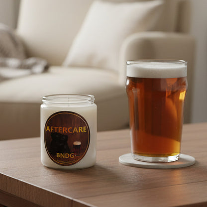 a candle jar with "Aftercare"-scent on a table with a glass of beer and a cozy sofa in the background 