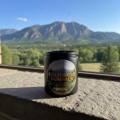 A black candle jar with "Colorado Summer"-scent on a stone window sill and the Flat Irons in the background