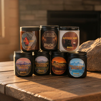 7 candle jars on a wooden table with a fireplace in the background
