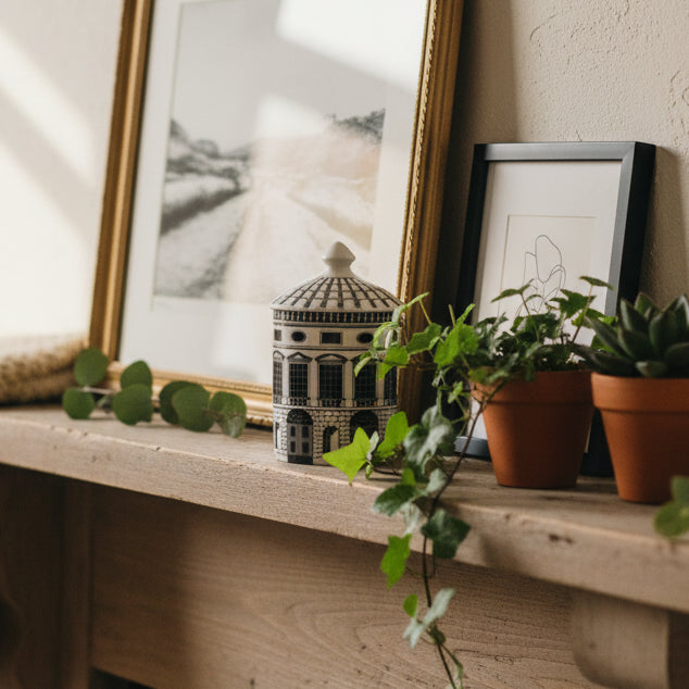 A small cylindrical lidded box or container with a detailed architectural building design in black and white, sitting on a mantle.