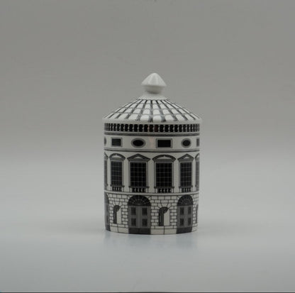 A small cylindrical lidded box or container with a detailed architectural building design in black and white, set against a plain gray studio background.