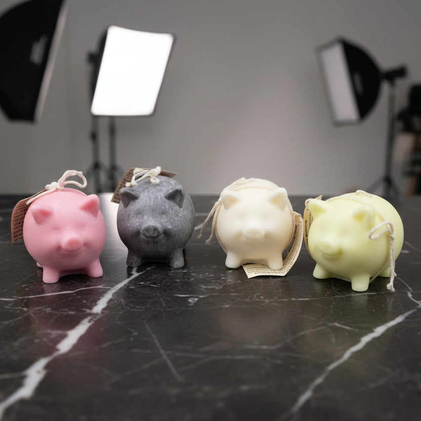 4 small pig candles (pink, black, white, and yellow) on a dark marble counter in a photo studio