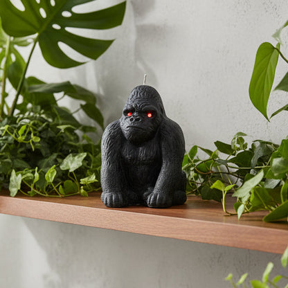 A black gorilla-shaped novelty candle with orange eyes, on a shelf with plants