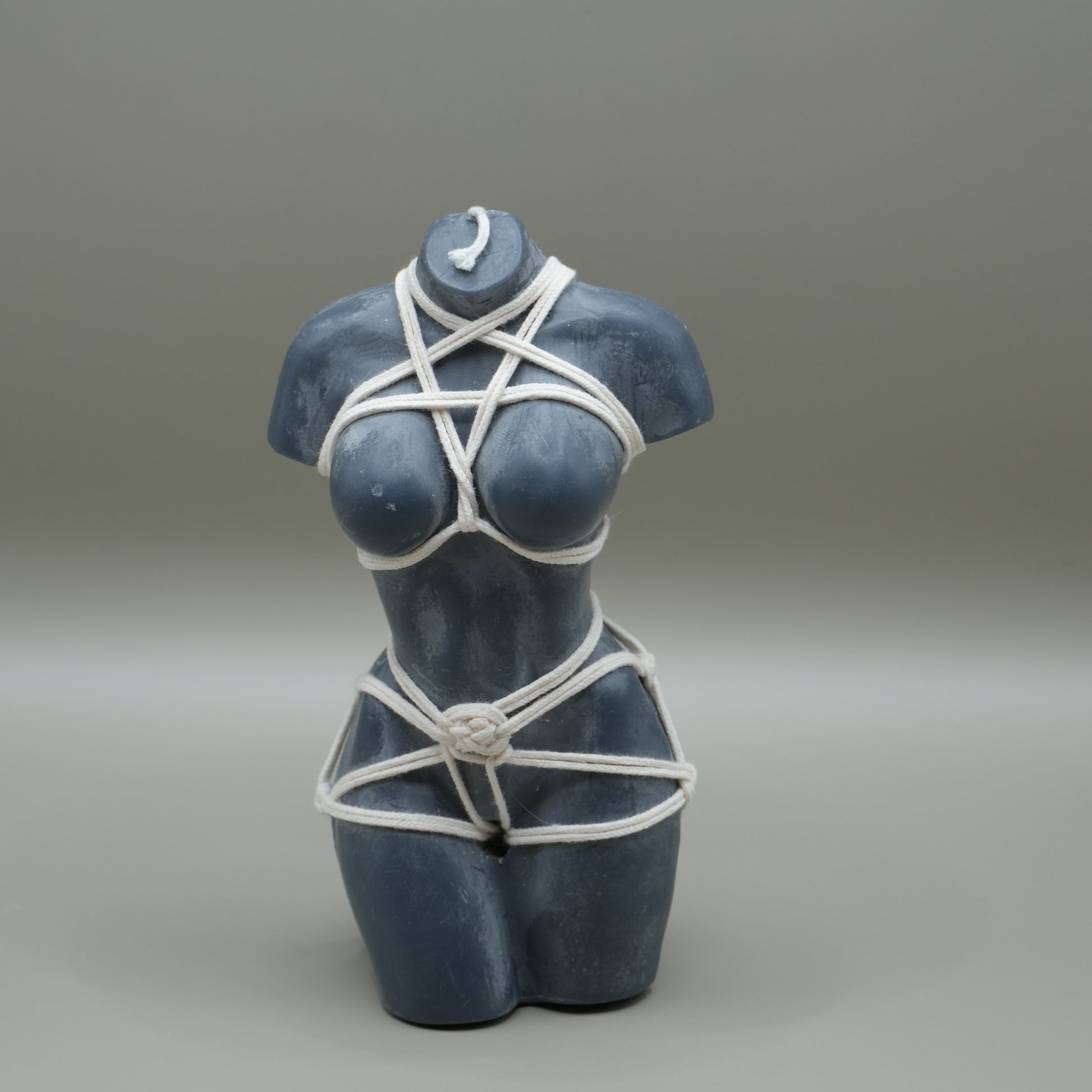 a dark grey female torso candle with white shibari rope harness 