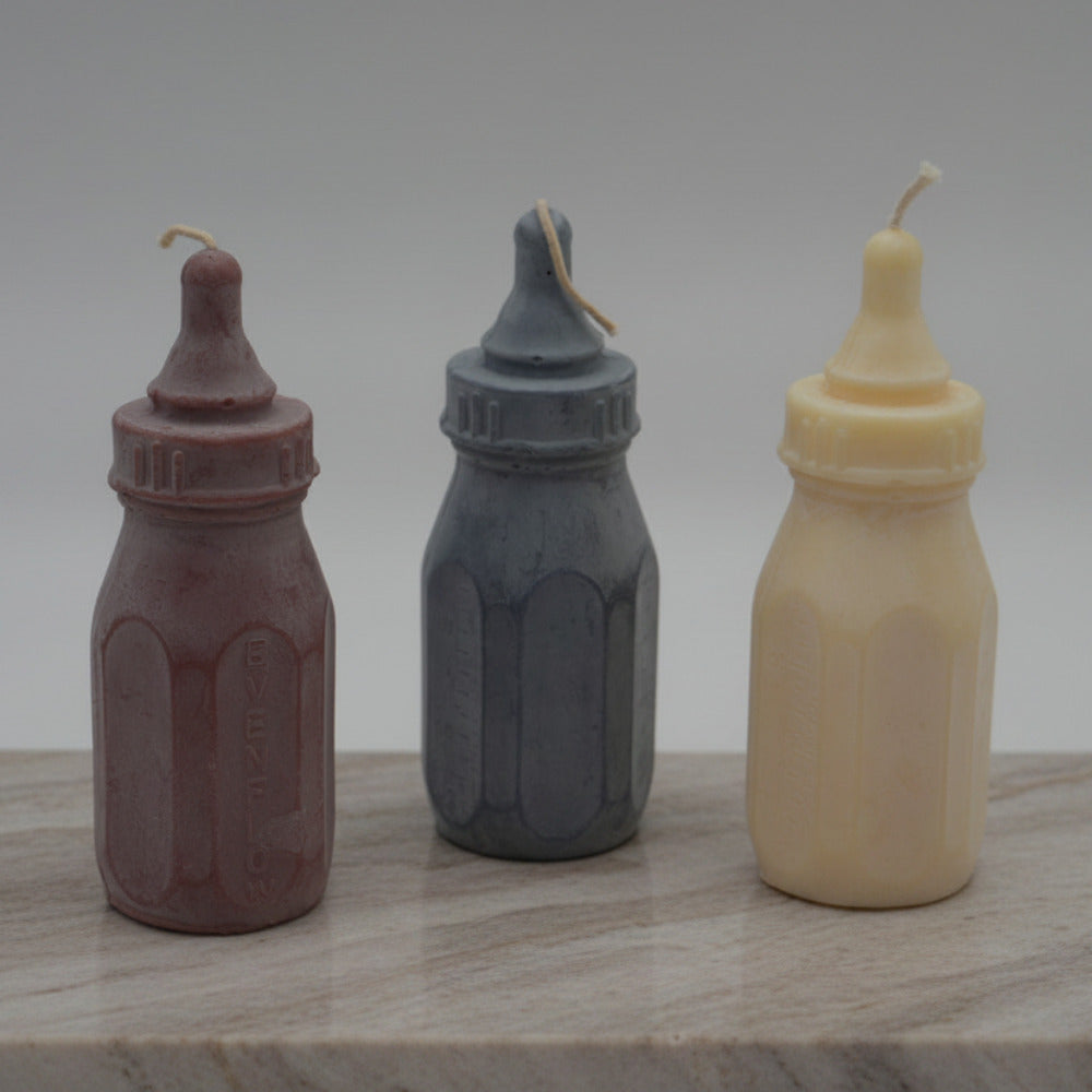 Three Baby bottle candles on a stone surface with grey background