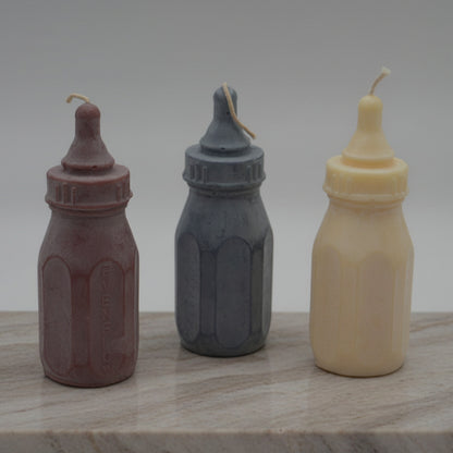 Three Baby bottle candles on a stone surface with grey background