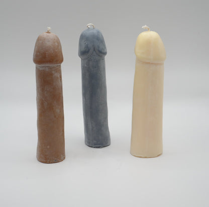 three penis pillar candles (brown, dark grey, and white) on light grey background