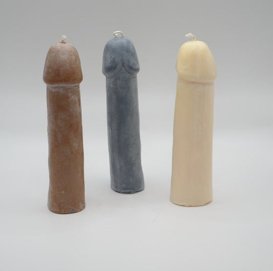 three penis pillar candles (brown, dark grey, and white) on light grey background