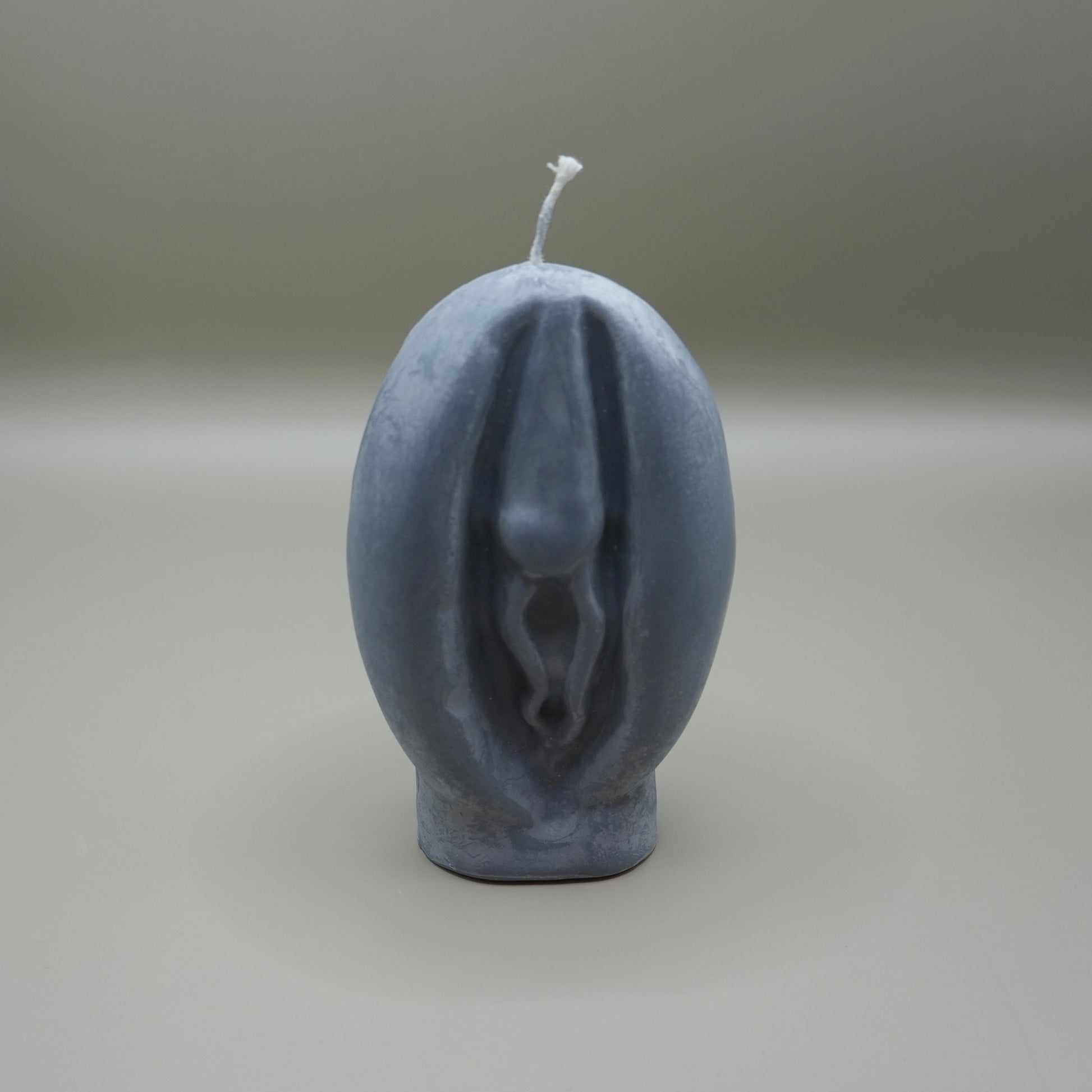 a dark grey vagina-shaped candle on grey background