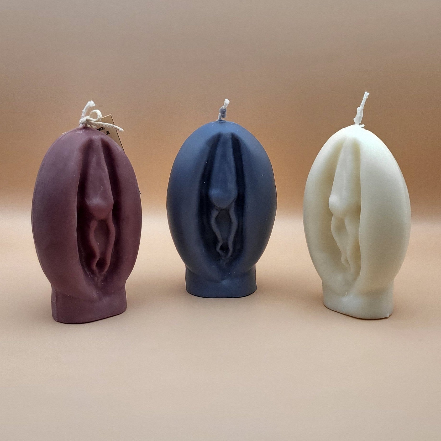 3 Vagina candles (Brown, black, white) with a beige background