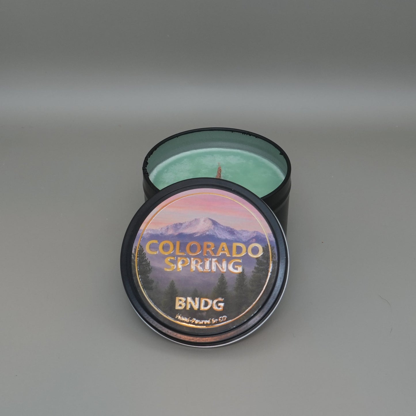 Candle tin with "Colorado Spring"-scent with a gray back ground