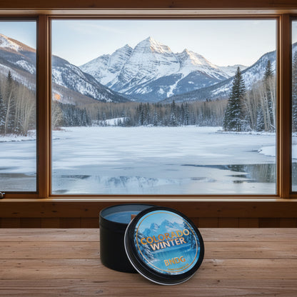 a candle tin with "Colorado Winter"-scent on a table with the maroon bells and a frozen lake