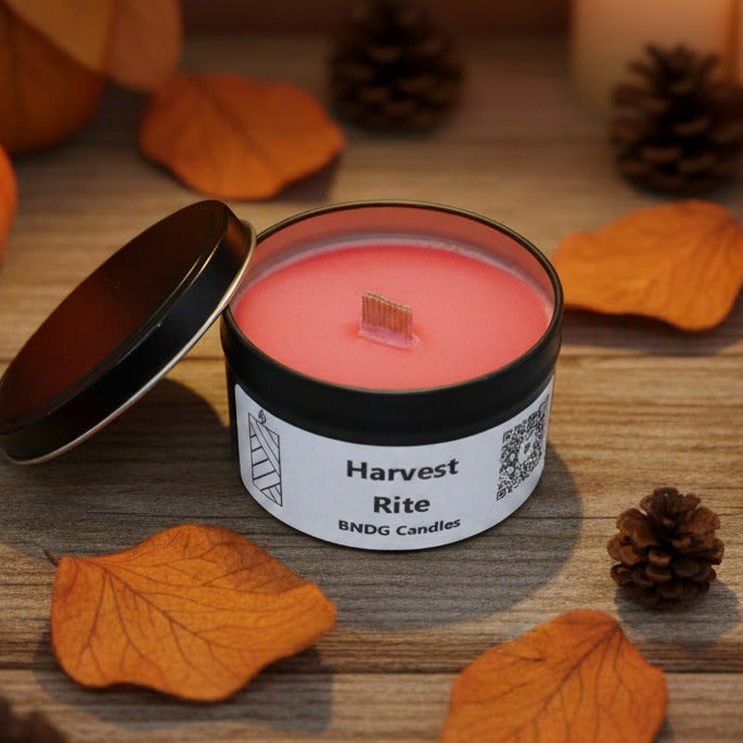 A candle tin with "Harvest Rite"-scent on a wooden tale with fall leaves and pine cones
