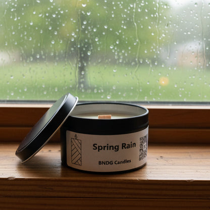 Candle tin with "Spring Rain"-scent on a window sill with rain outside