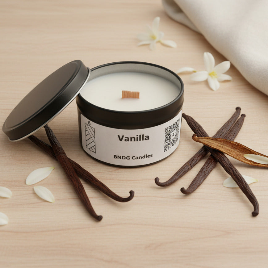 a "vanilla"-scented candle tin on a table, surrounded by vanilla beans, flowers and a towel on the side 