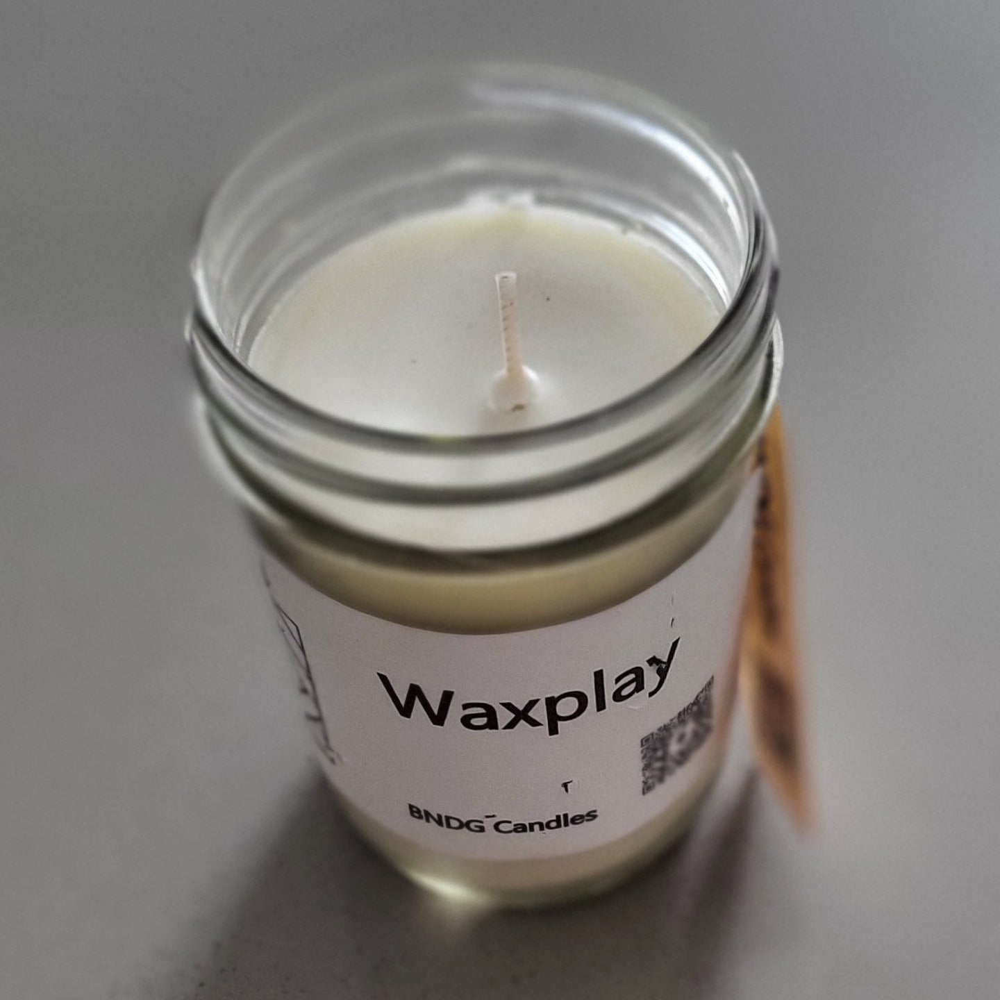 Small candle in a glass jar with a label on a gray surface